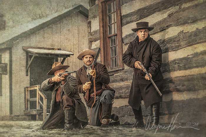 Three cowboys stand ready on the porch of a weathered frontier cabin, rifles in hand, eyes sharp for what’s coming. By Wayne Heim.